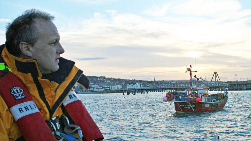 Swanage assistant mechanic Colin Marks stood by the shore, sunset in the distance.