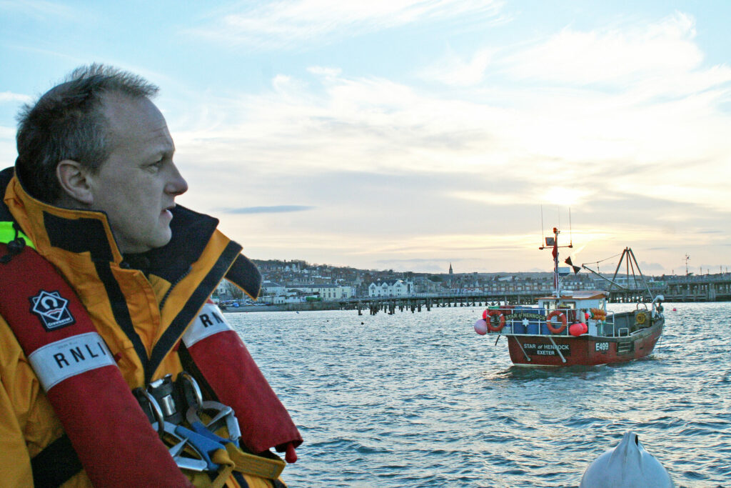 Swanage assistant mechanic Colin Marks stood by the shore, sunset in the distance.